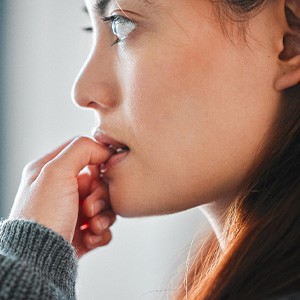 Profile view of woman gazing out window biting thumbnail
