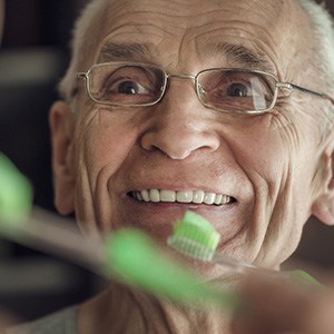 An older man brushing his teeth in front of a bathroom mirror