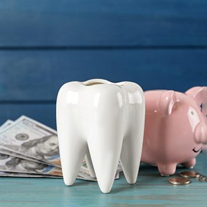 A large ceramic tooth model next to a piggy bank and dollar bills